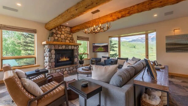 Ein gemütliches Wohnzimmer mit Kamin aus Stein, Ledersofas und großen Fenstern mit Blick ins Freie.