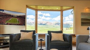 Ein Wohnzimmer mit zwei dunklen Sofas, einem Couchtisch und einem Fernseher, der ein Fußballspiel zeigt.