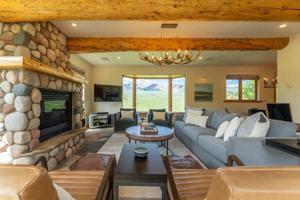 Una sala de estar con chimenea de piedra, un sofá grande, un televisor y vistas al exterior.