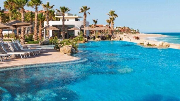 A resort with a large pool, palm trees, and a beach.