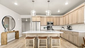 A modern kitchen with a central island, wooden bar stools, stainless steel appliances, and light wood cabinetry.