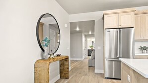 A modern kitchen with wooden cabinets, a stainless steel refrigerator, and a wooden console table with a mirror.