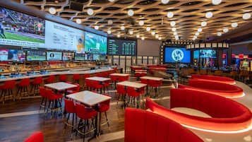 A modern bar area with multiple screens displaying sports content, red seating, and a unique ceiling design.