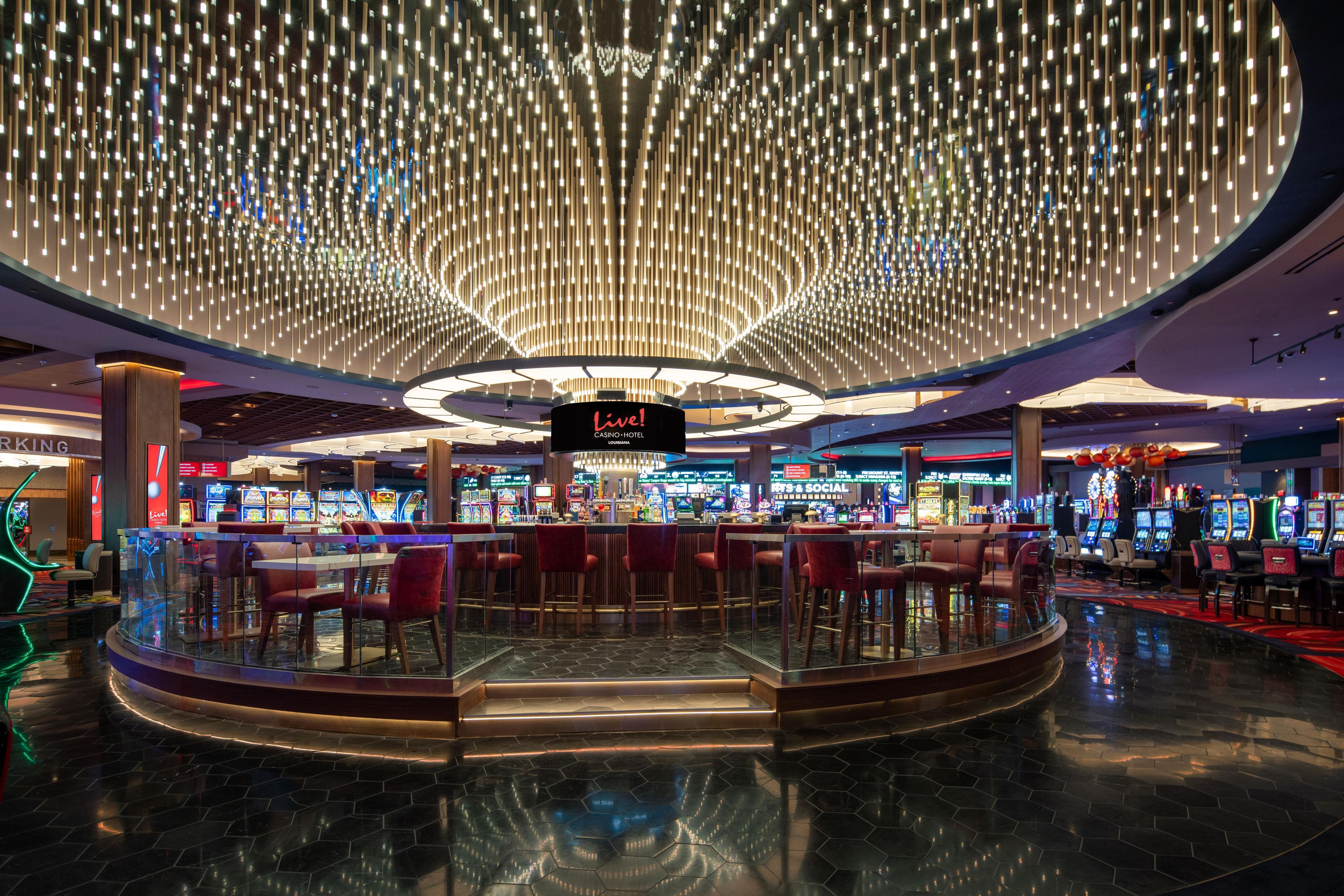 A casino with a central bar area, gaming machines, and a modern ceiling design.