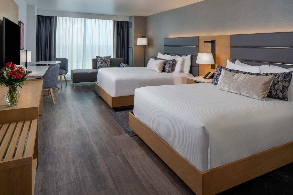Una habitación de hotel con dos camas, un escritorio, una silla, un televisor y un ventanal con cortinas.
