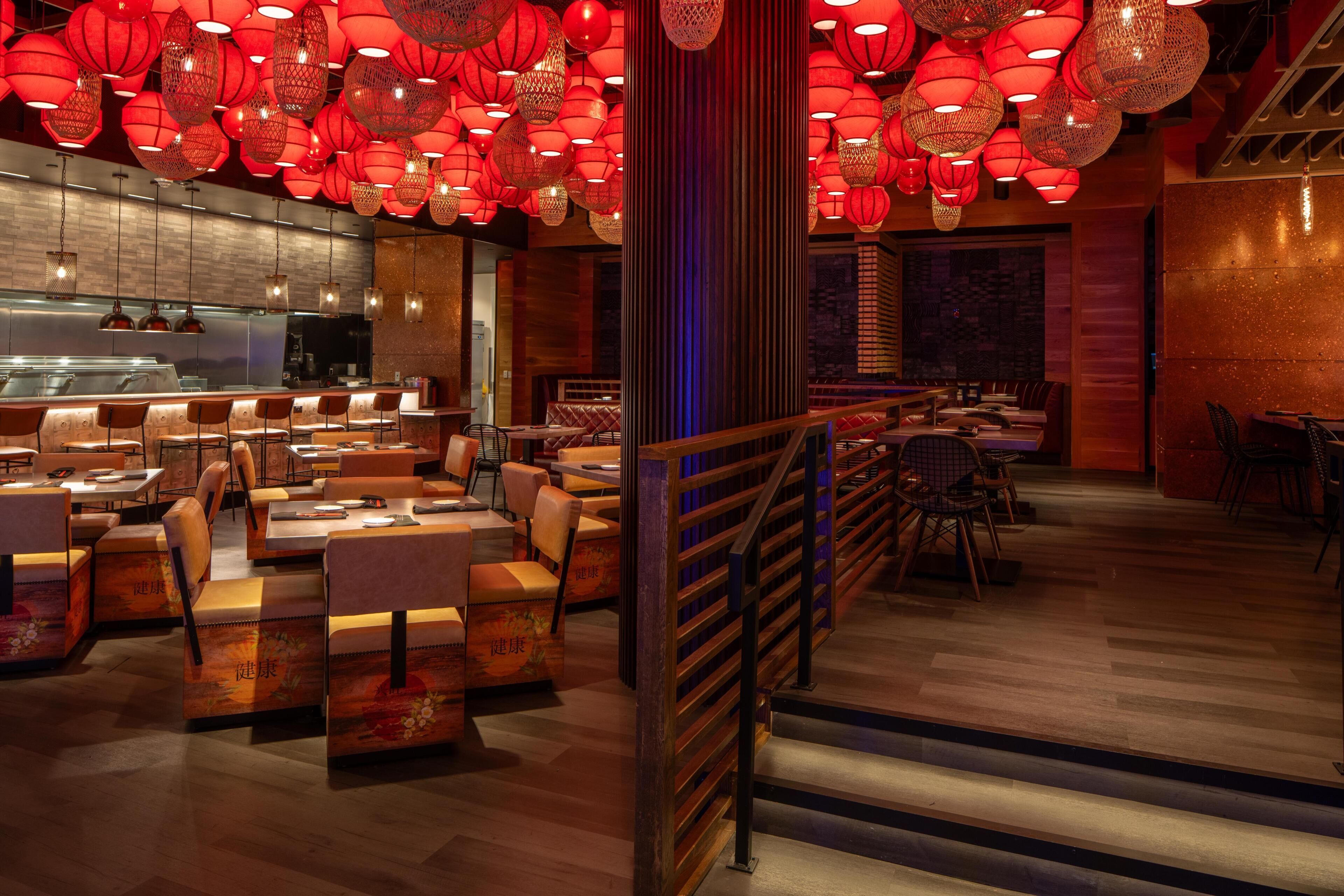 Interior de restaurante con varias mesas y sillas, una escalera y faroles rojos colgantes.