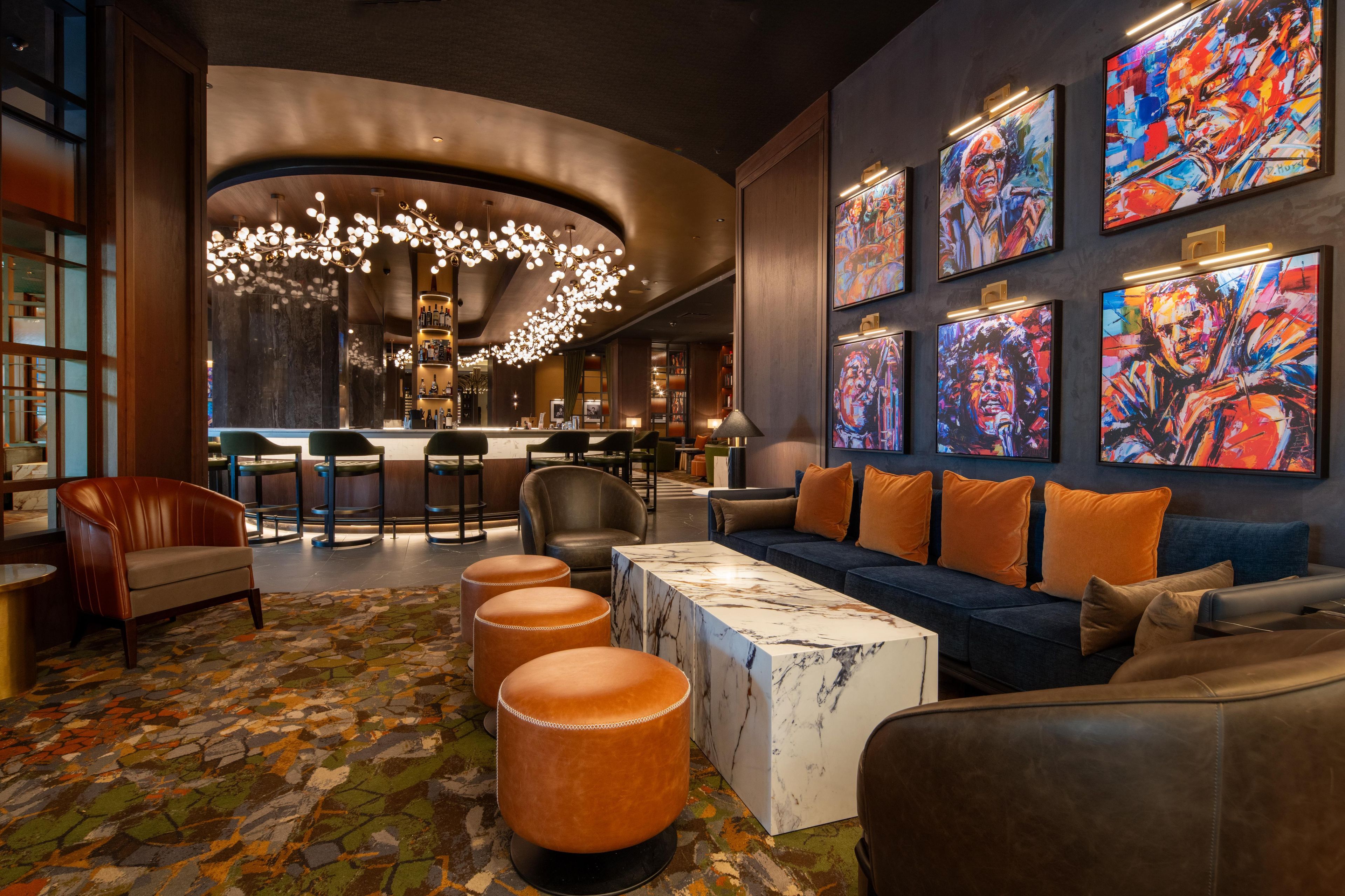 Un espace lounge moderne doté d’un plafond incurvé, de sièges au bar, d’un canapé avec des coussins orange et d’œuvres d’art abstraites accrochées aux murs.