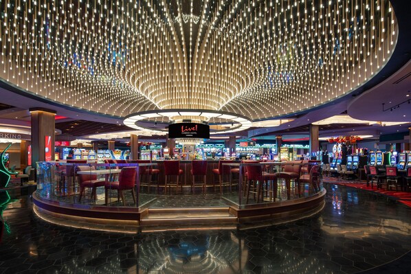 Un casino con una barra central, múltiples máquinas de juego y una lámpara de techo distintiva.