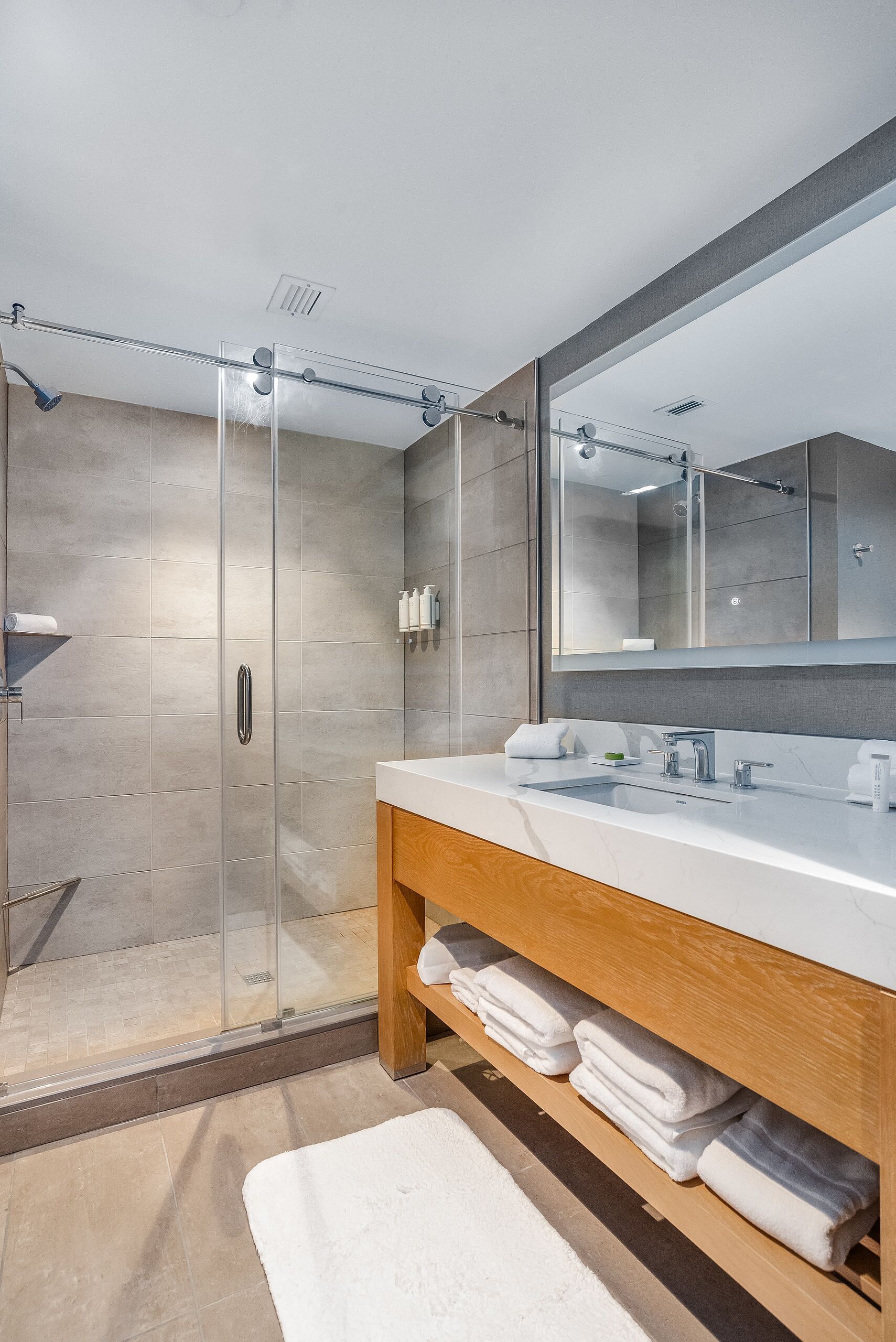 A modern bathroom with a glass-enclosed shower, a large mirror, and a wooden vanity with towels.