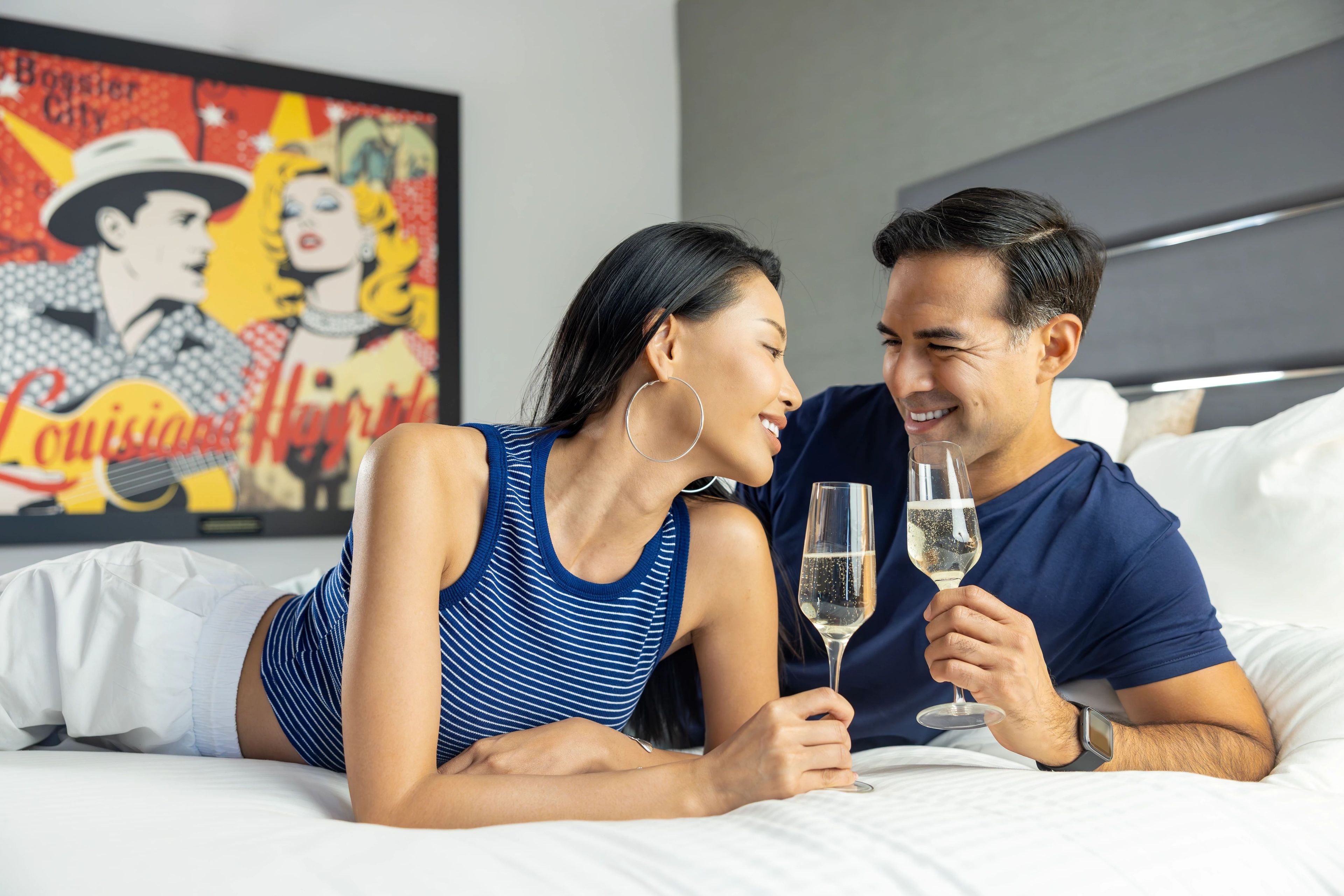 Um casal deitado em uma cama, com um quadro ao fundo.