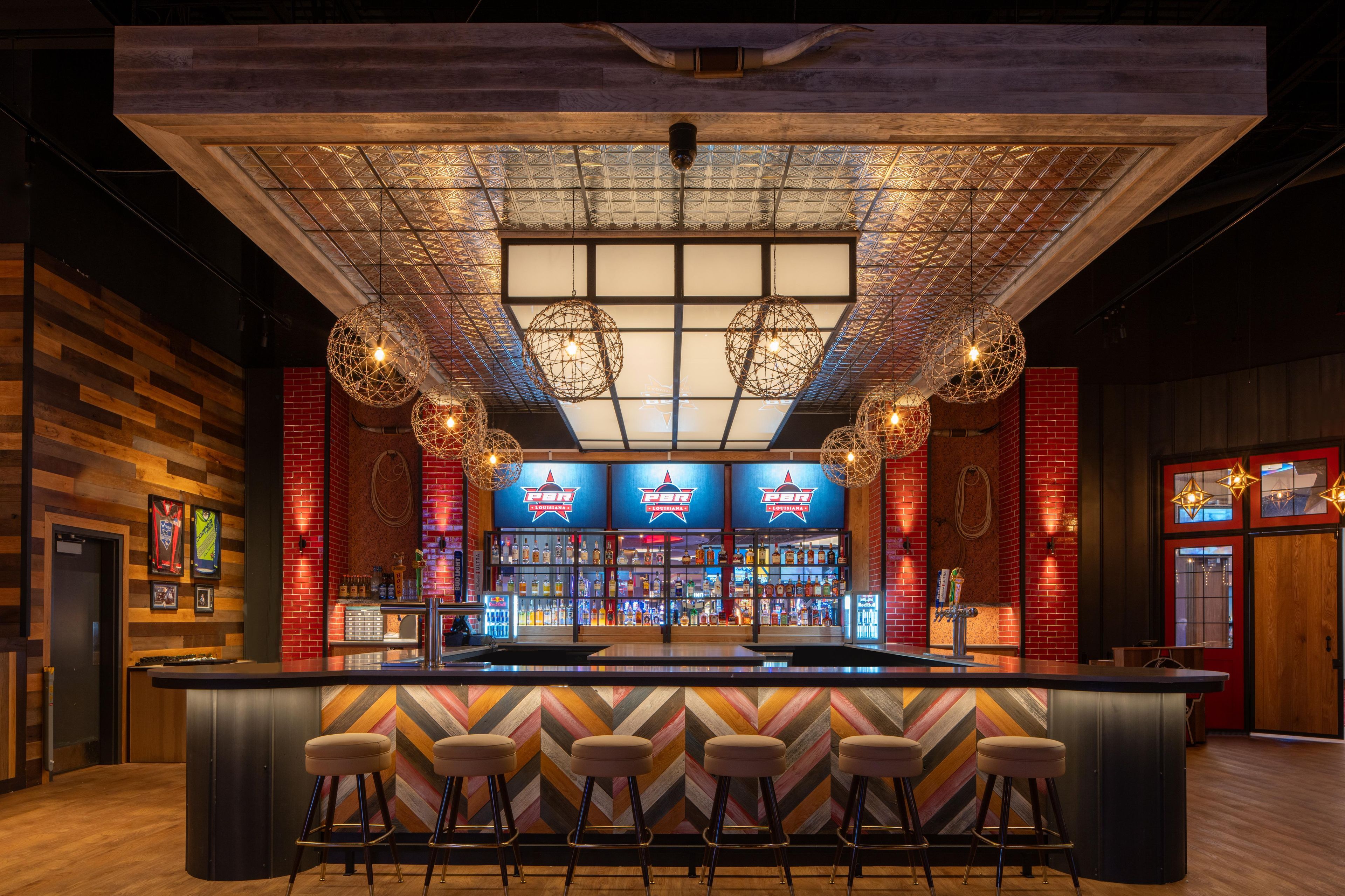 A bar area with a central counter, multiple stools, and hanging spherical light fixtures.