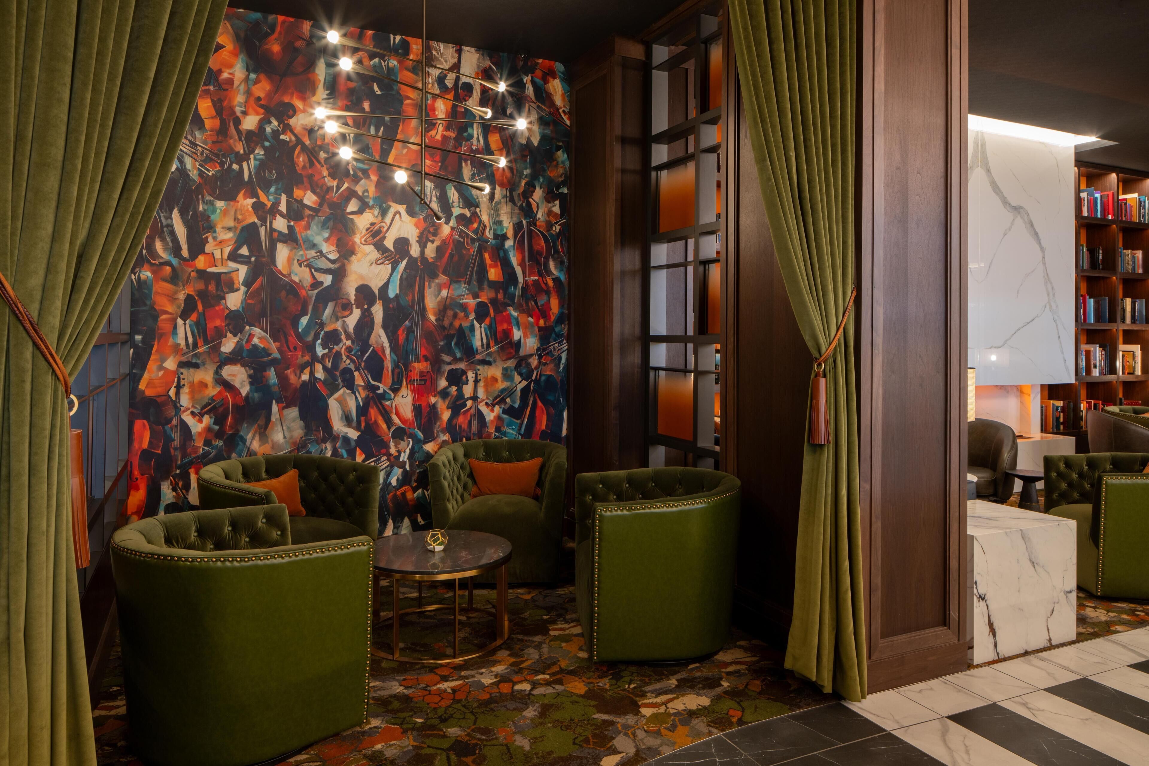 A room with green upholstered chairs, a marble coffee table, a colorful abstract mural, and a bookshelf.