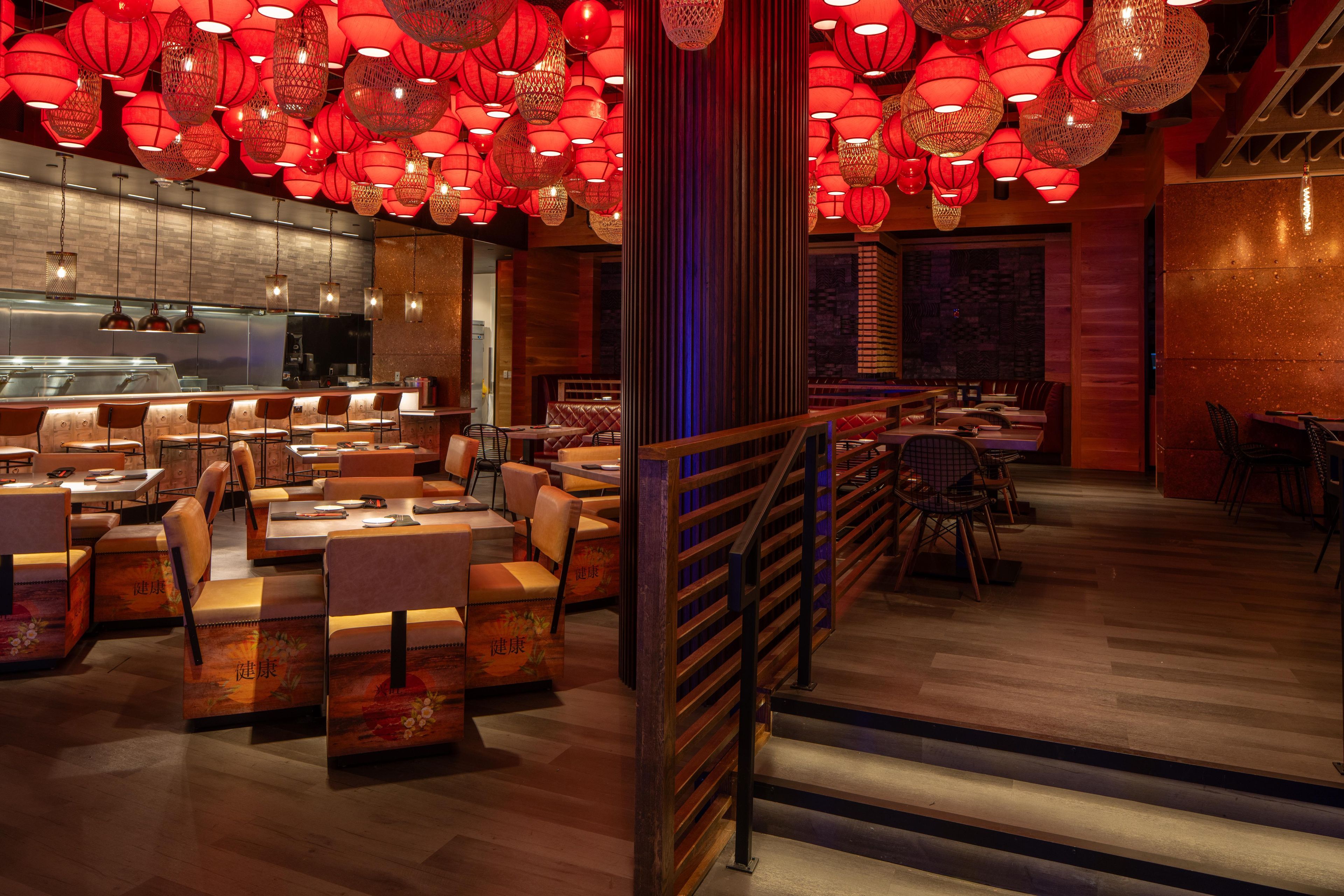 A restaurant interior with multiple dining tables and booths, a kitchen area, and red hanging lanterns.