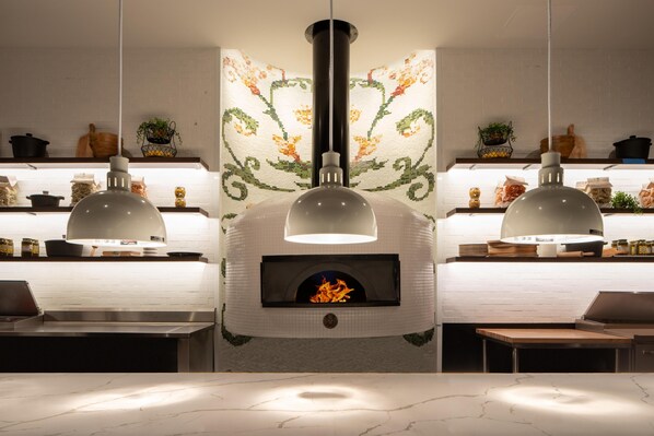 A modern kitchen with a central wood-fired oven, pendant lighting, and a white brick backsplash. - Live Casino Hotel Bossier (Bossier City)