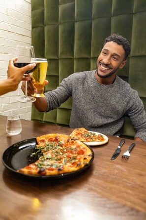 A person seated at a table with a pizza and a glass of beer.