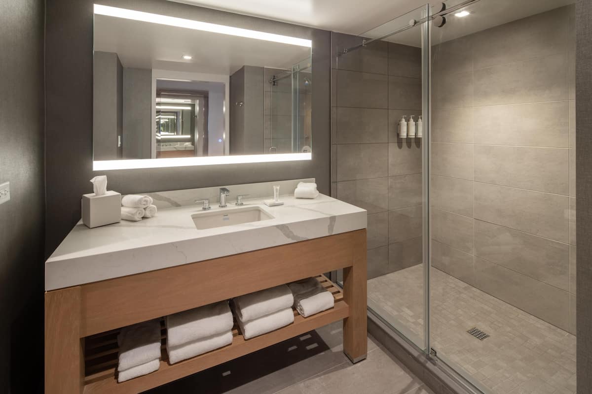 Un baño moderno con un espejo grande, dos lavamanos, cabina de ducha de vidrio y un mueble de tocador de madera con toallas.