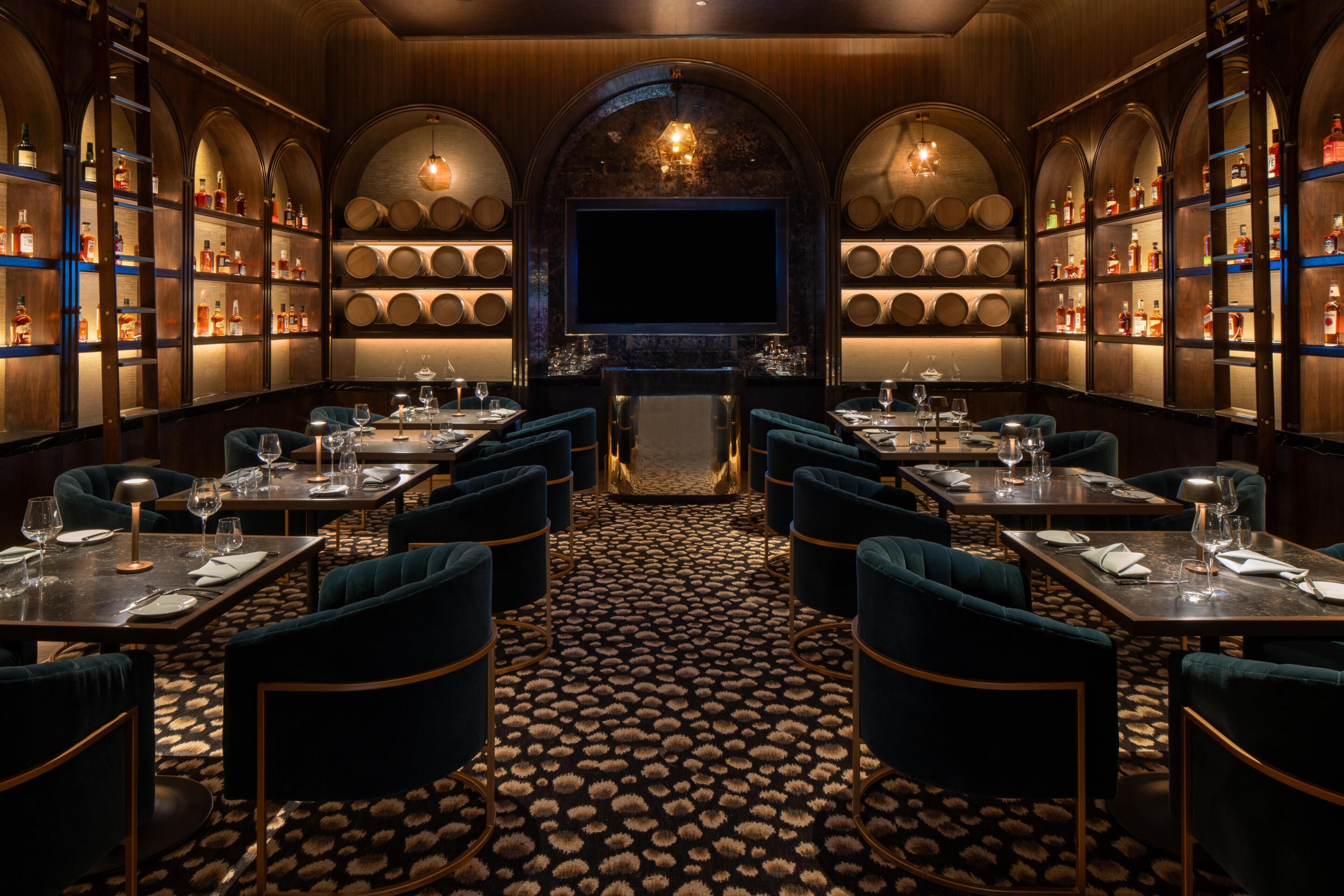 A restaurant with a central bar area, multiple tables with chairs, and shelves with bottles.