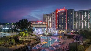 Un complejo de casino y hotel con área de piscina, mobiliario exterior y un llamativo letrero que dice 'Live!'.