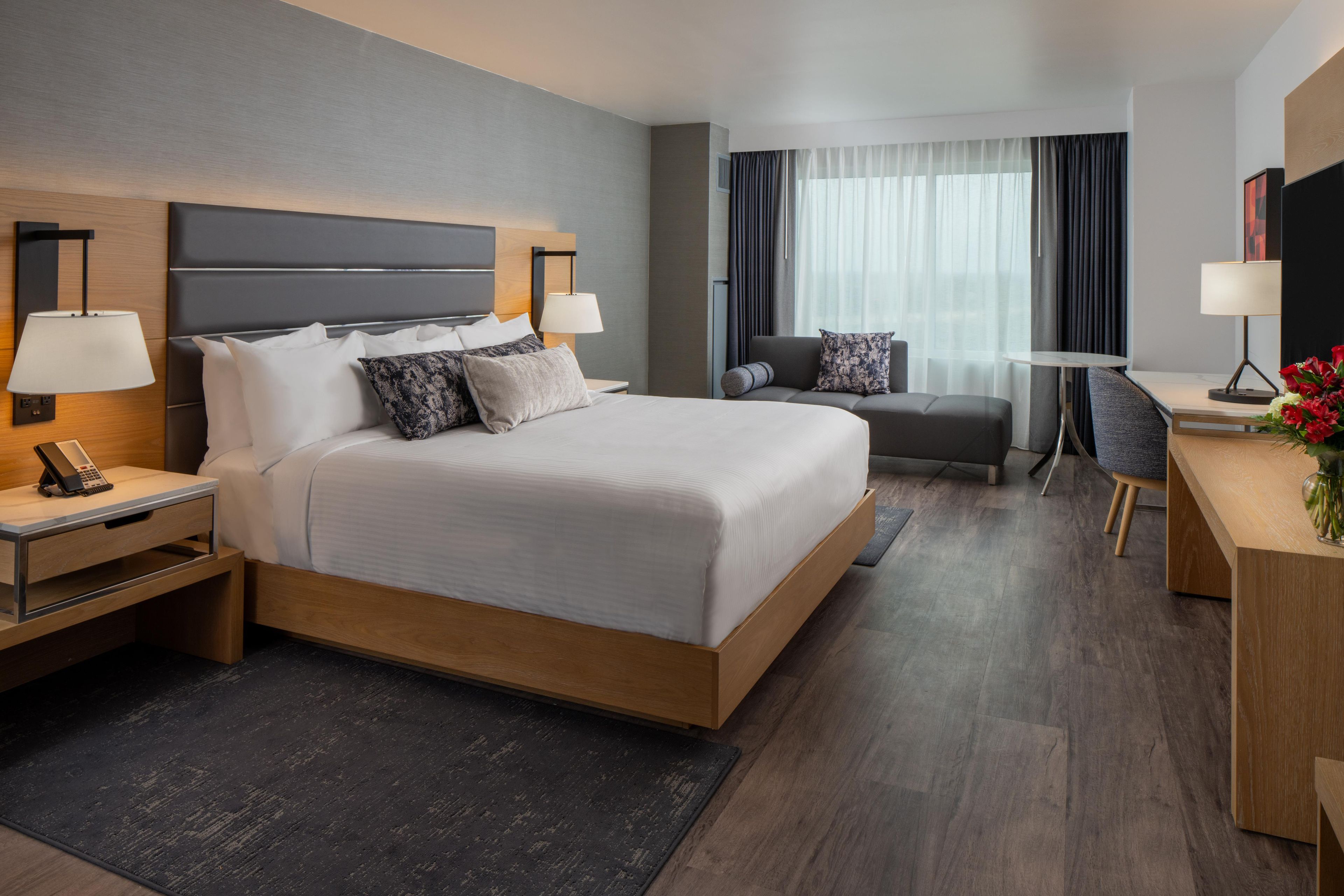A hotel room with a large bed, bedside tables, a desk, a chair, and a small table with a lamp.