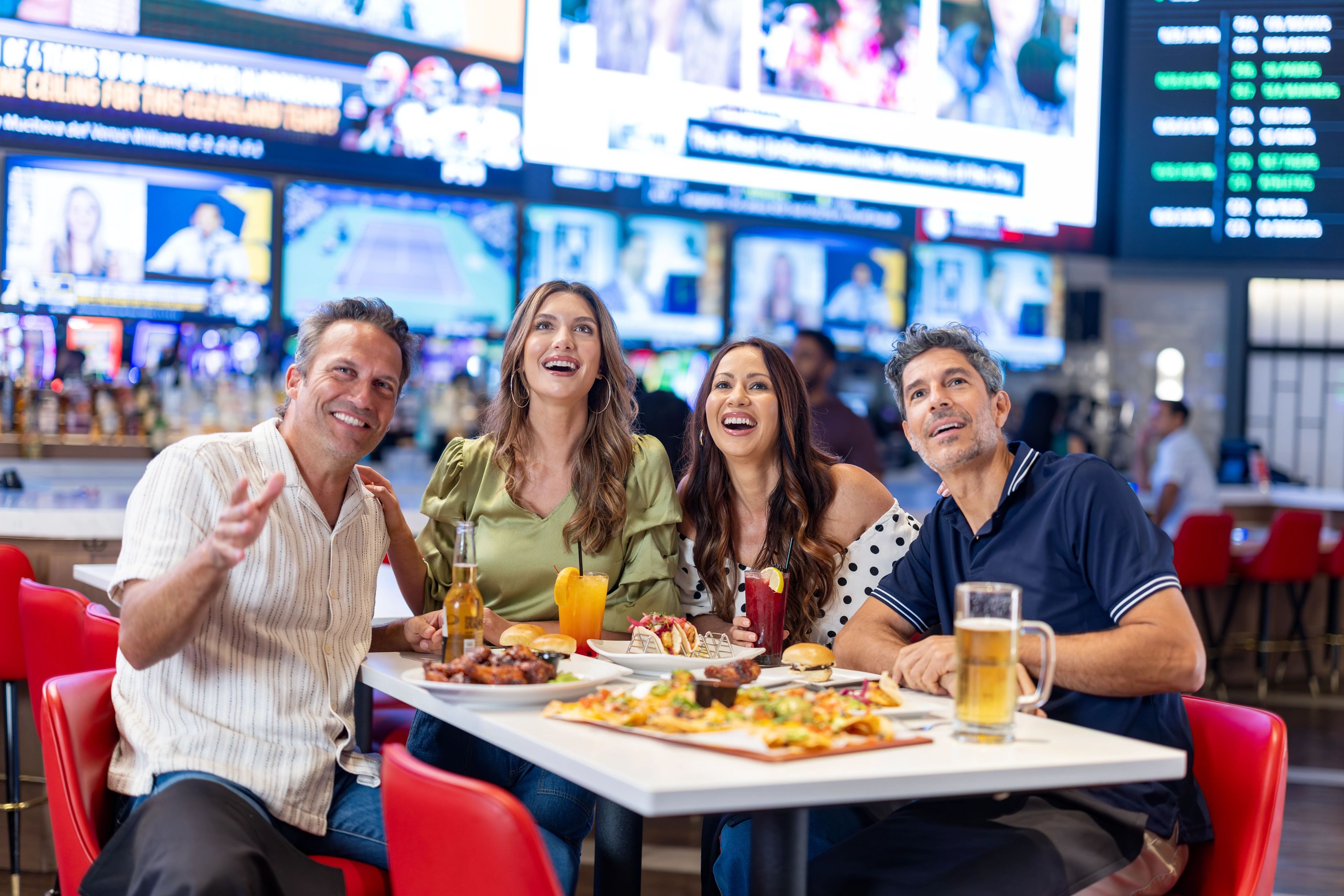 Un grupo de personas sentadas en una mesa en un bar o restaurante, con una pantalla mostrando deportes al fondo.