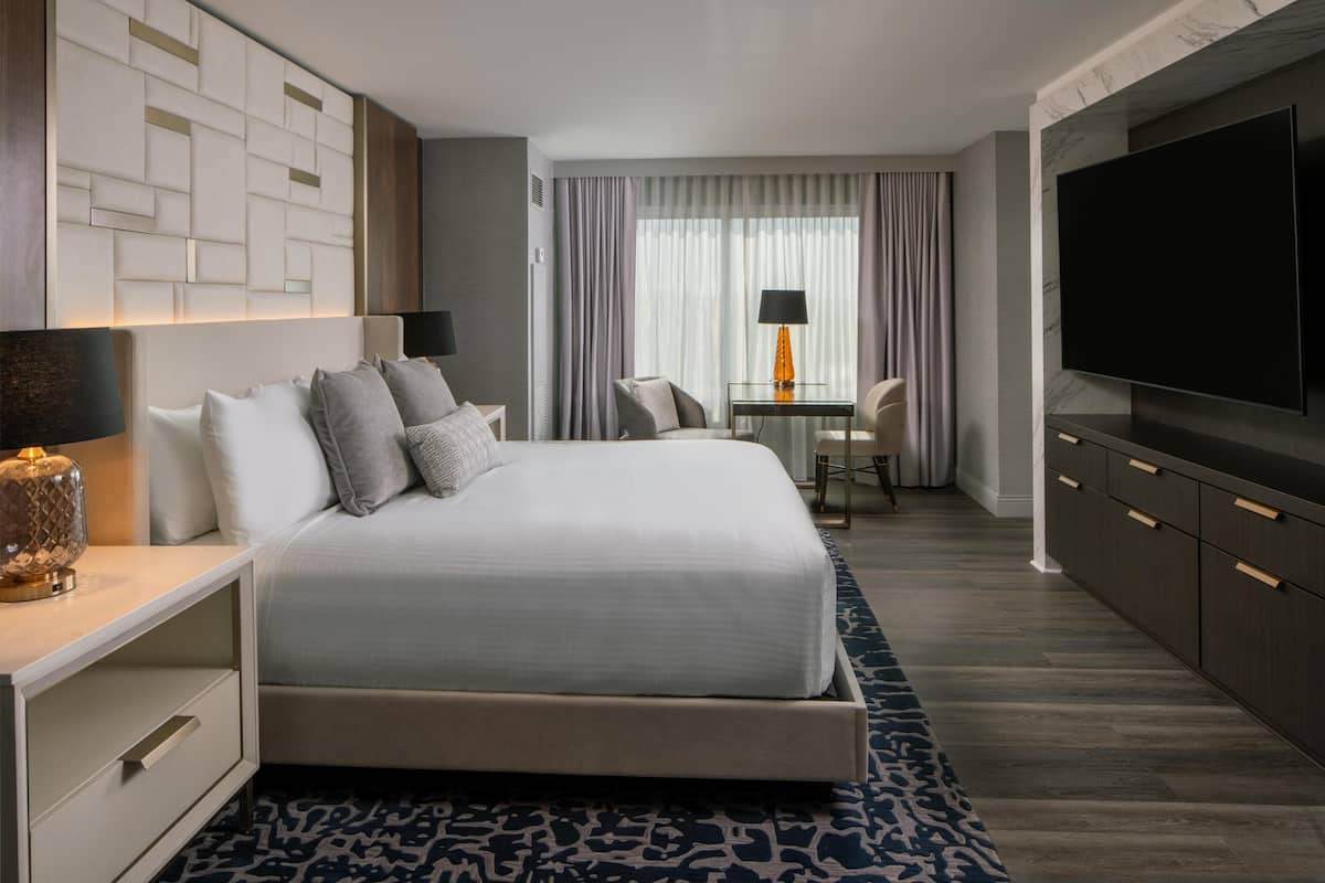 Habitación de hotel moderna con una cama grande, mesitas de noche, un escritorio con silla, televisión de pantalla plana y vistas al exterior a través de la ventana.