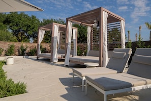 A patio area with two wooden pergolas, cushioned lounge chairs, and a round table. - Live Casino Hotel Bossier (Bossier City)