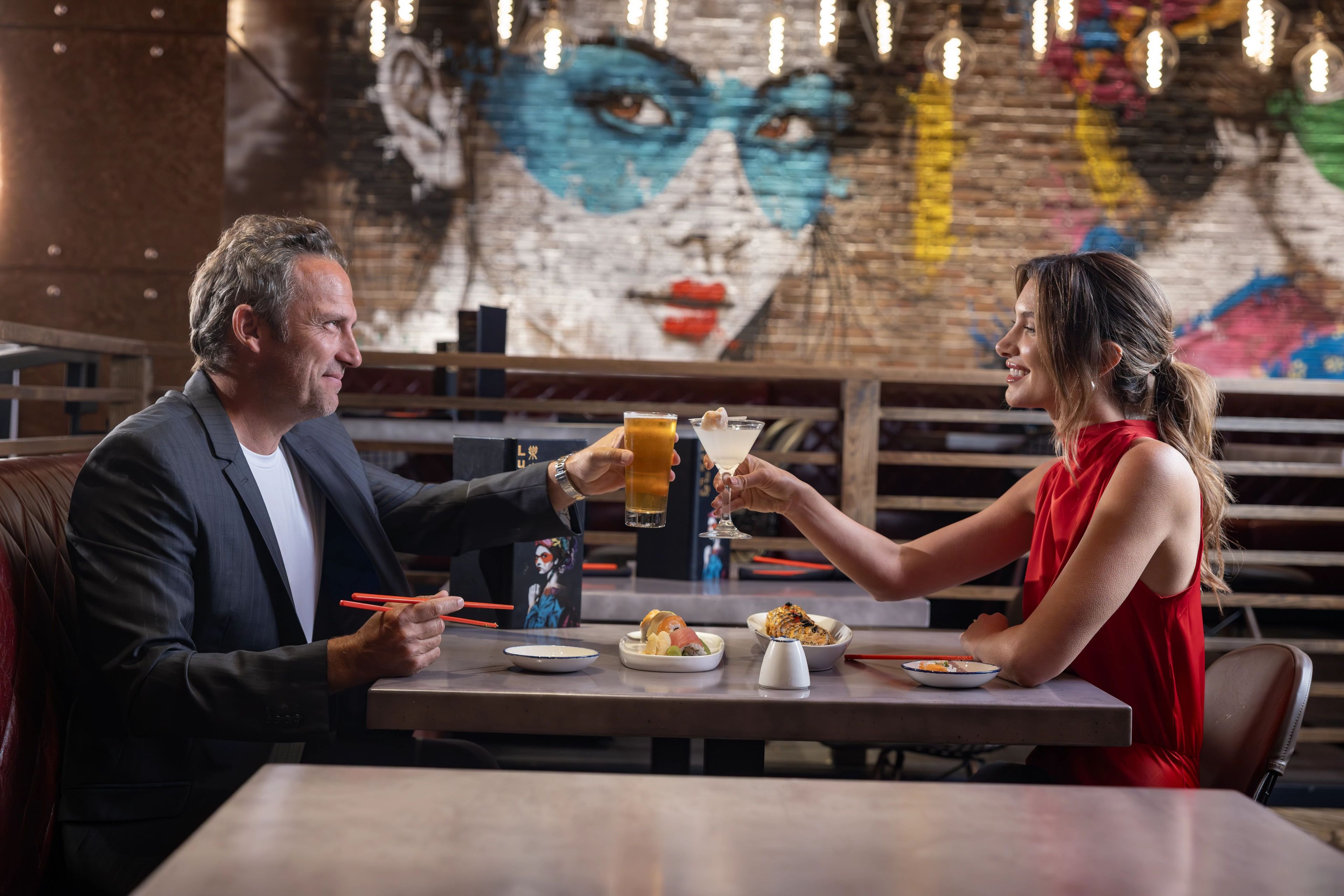 Un homme et une femme sont assis à une table dans un restaurant, avec une fresque murale en arrière-plan.