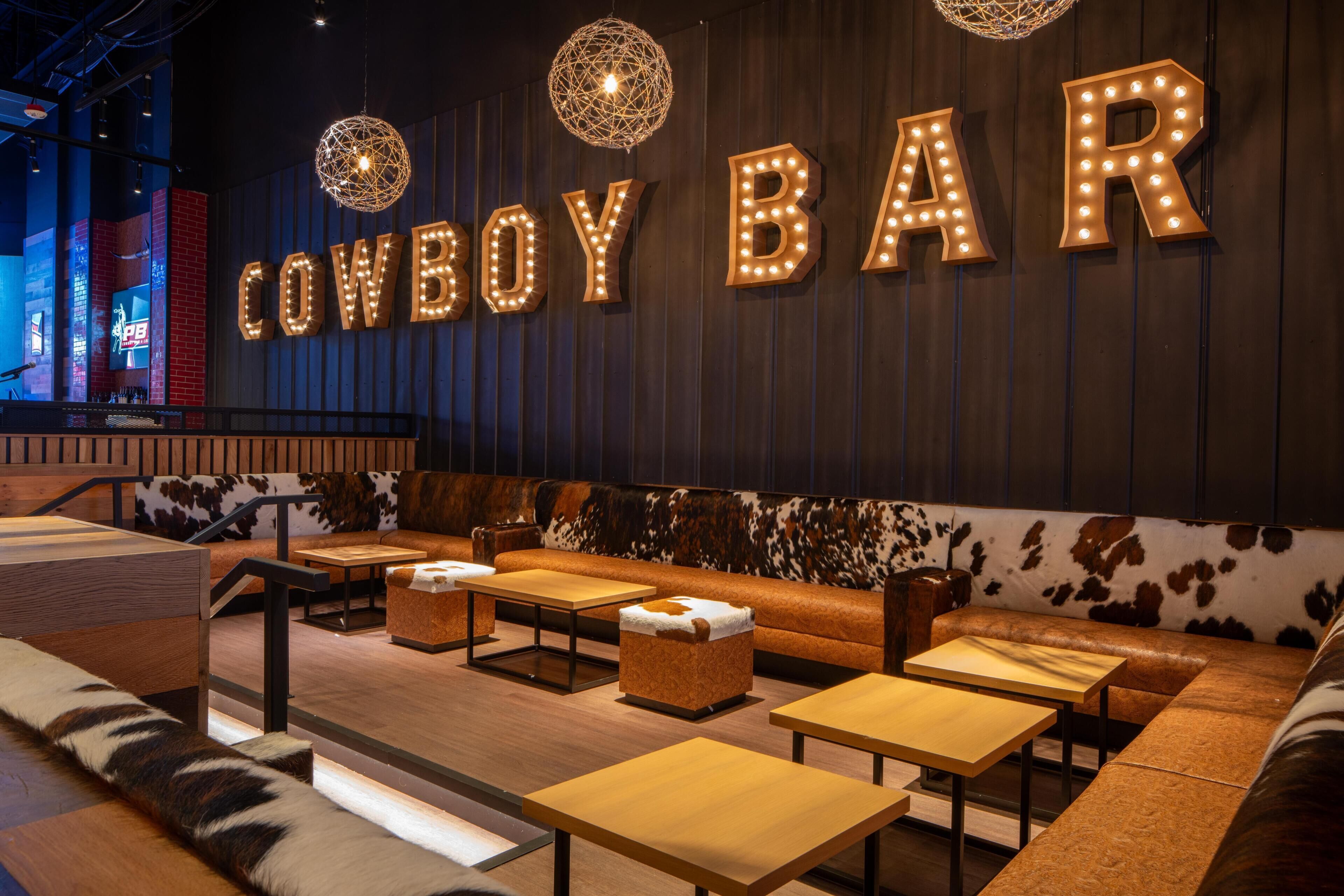 A bar area with a cowhide wall, leather seating, and illuminated letters spelling 'COWBOY BAR'.