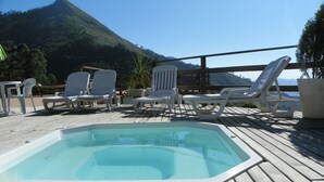 A wooden deck with a hot tub and white lounge chairs. - Hotel Caledônia Inn (Nova Friburgo)