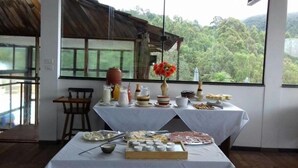A dining area with a table set for a meal, featuring various food items and a vase with flowers. - Hotel Caledônia Inn (Nova Friburgo)
