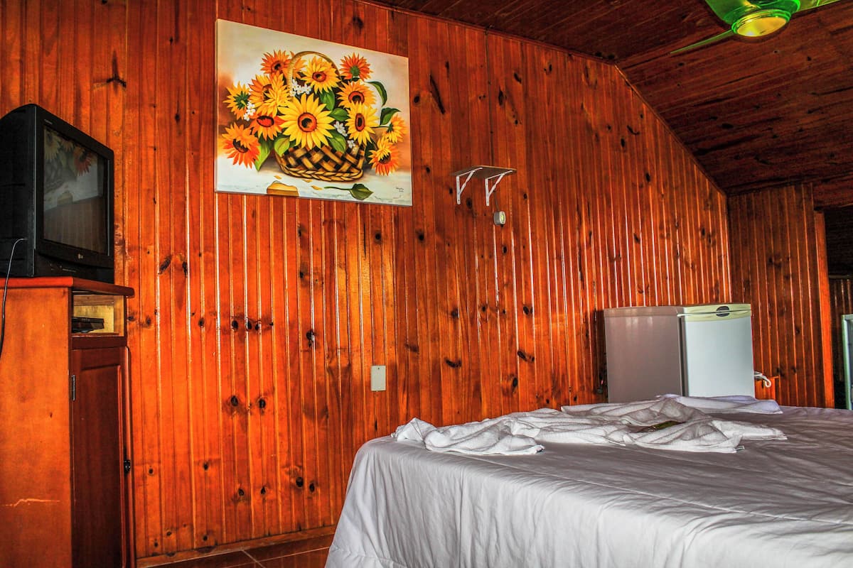 Ein Zimmer mit Holzwänden, einem Bett, einem Fernseher und einem Kühlschrank.
