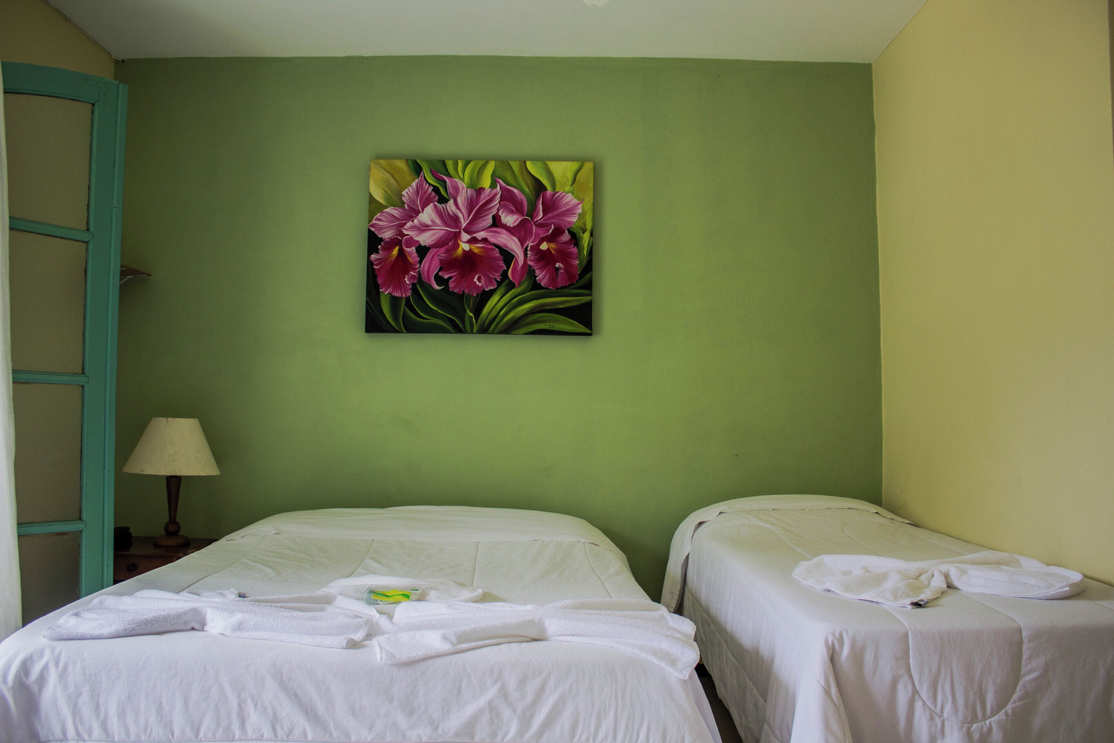 A hotel room with two beds, a green wall, and a painting of flowers.
