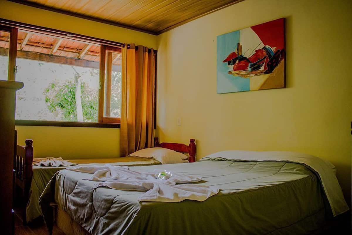 Ein Zimmer mit zwei Betten, einem Vorhangfenster, einem Bild an der Wand und einer Holzbalkendecke.