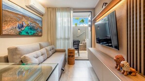 Een moderne hotelkamer met een bank, een flatscreen televisie, een decoratieve houten kruk en een schilderij van een kustlandschap.