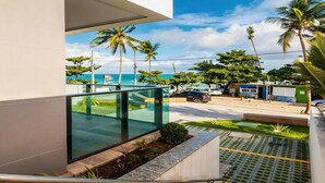 Een modern gebouw met een glazen balkon dat uitkijkt over een strand en palmbomen.
