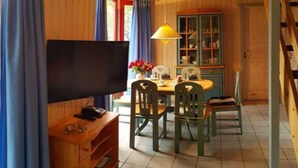 Un intérieur en bois avec un téléviseur posé sur un meuble en bois, une table à manger avec des chaises, une lampe et un buffet avec des portes en verre.