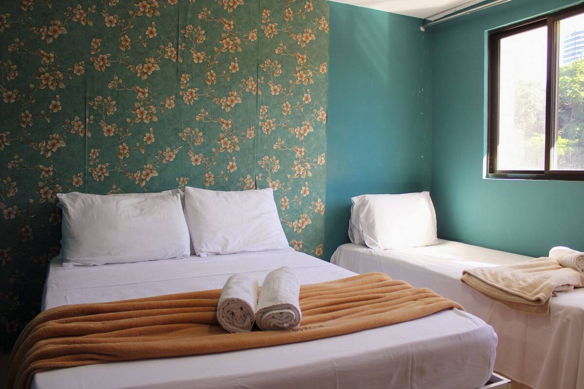 A hotel room with two beds, a window, and floral wallpaper.