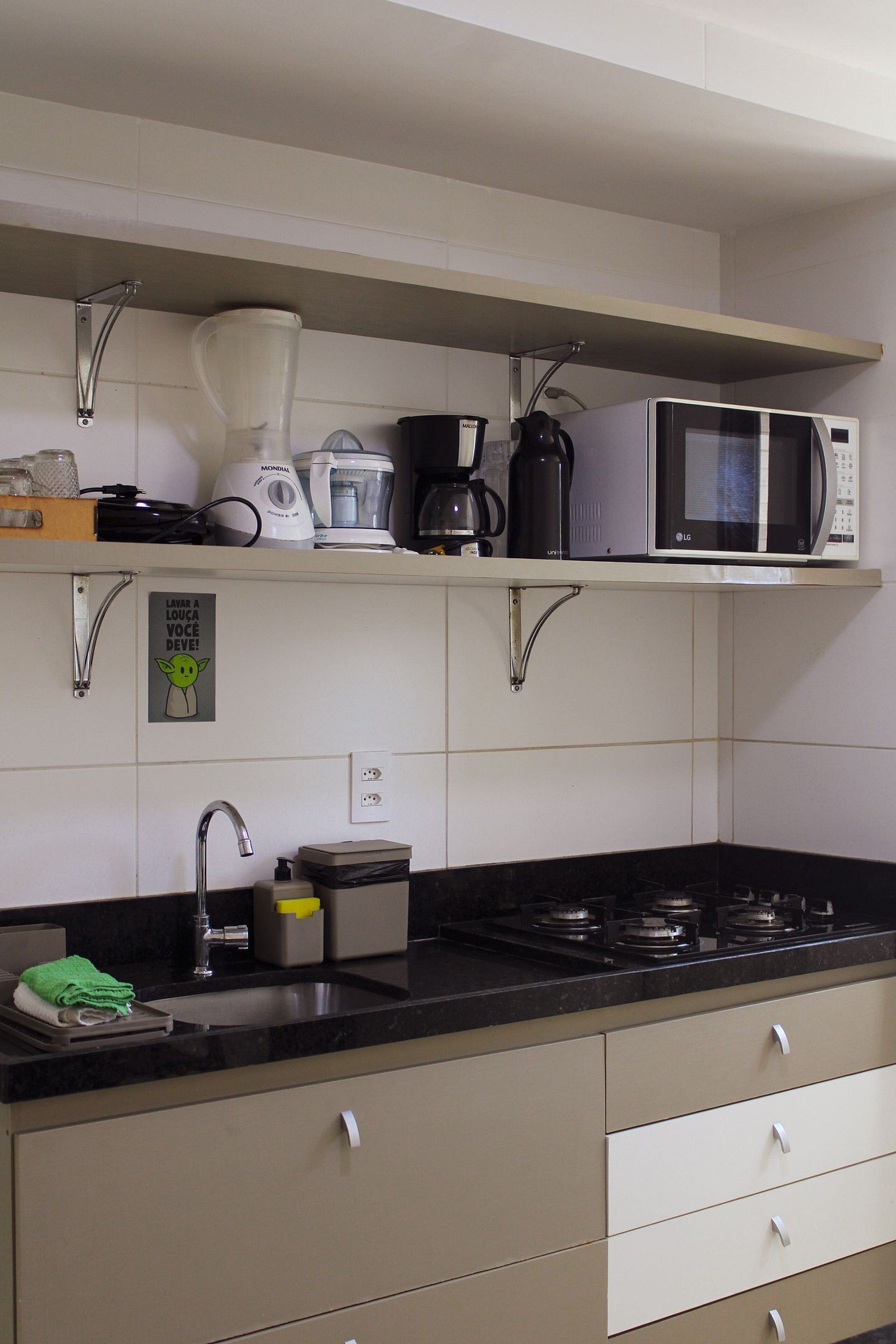 A kitchen with a black countertop, stainless steel sink, and a microwave above the stove.