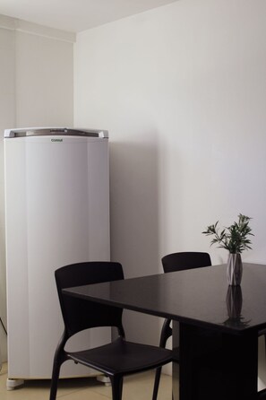 Una habitación con un refrigerador blanco, una mesa de comedor con dos sillas y un jarrón con una planta sobre la mesa.