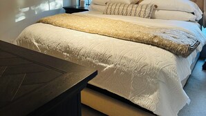 Un dormitorio con una cama grande, una mesita de noche, una lámpara y una ventana con persianas.