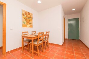 A dining area with a wooden table and chairs, a painting on the wall, and a green door in the background.