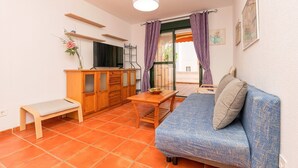 A small, cozy room with a wooden bench, a table, a sofa, and a TV.