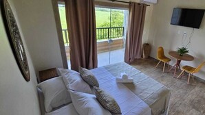 Ein Hotelzimmer mit Bett, Fernseher, einem Balkon mit Vorhängen und einem kleinen Tisch mit Stühlen.