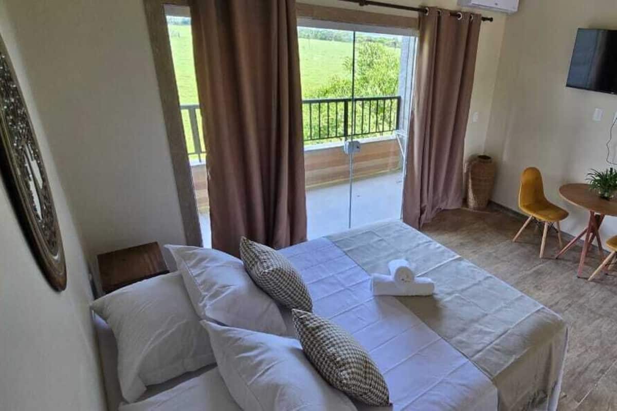 Hotelkamer met een bed, een televisie, een balkon met gordijnen en een klein tafeltje met stoelen.