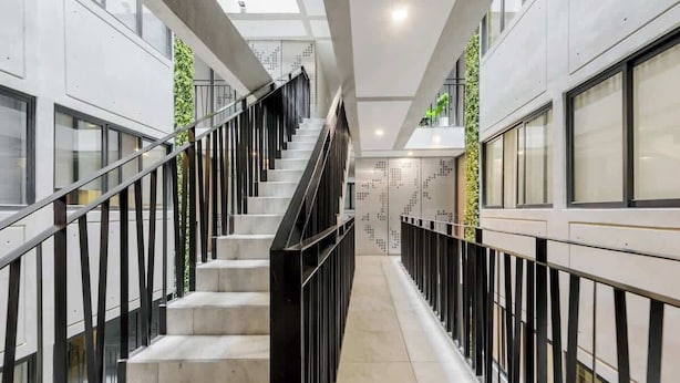 Un interior moderno con una escalera, barandales de vidrio y una pared con diseño geométrico.