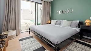 Un dormitorio con cama, dos mesitas de noche con lámparas, un ventanal con cortinas y una pared verde decorada con fases lunares.