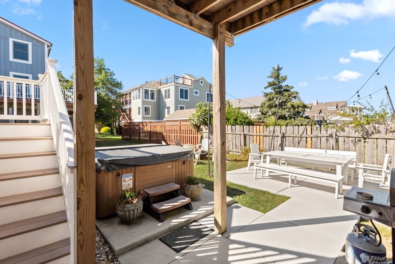 A covered patio with a hot tub, outdoor seating, and a barbecue grill.