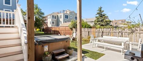 A covered patio with a hot tub, outdoor seating, and a barbecue grill.