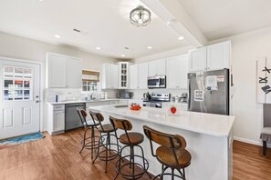 A modern kitchen with white cabinetry, stainless steel appliances, and a central island with bar stools.