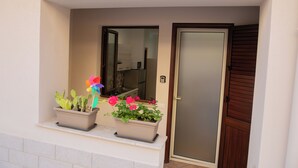 Un balcón con dos macetas, una con cactus y otra con flores rosas, y una puerta corrediza de vidrio a la derecha.
